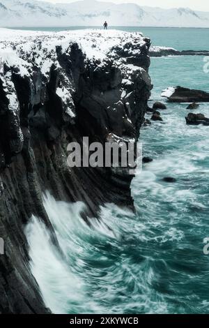 Randonneur solitaire au sommet des falaises de colonnes rocheuses basaltiques du volcan sur le rivage de l'océan Atlantique, à Arnastapi Islande, pendant l'hiver, aventure, voyage, Banque D'Images