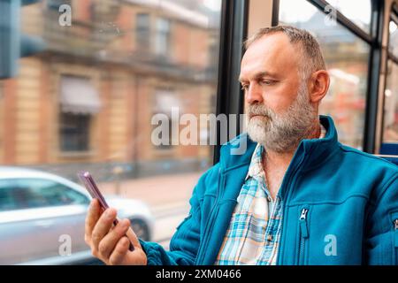 portrait d'un homme barbu dans une veste bleue parlant au téléphone dans un bus ou un tram. Concept de style de vie Banque D'Images