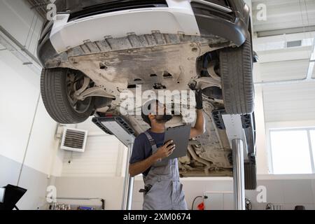 Auto mécanicien inspectant la voiture sur ascenseur hydraulique dans le garage Banque D'Images