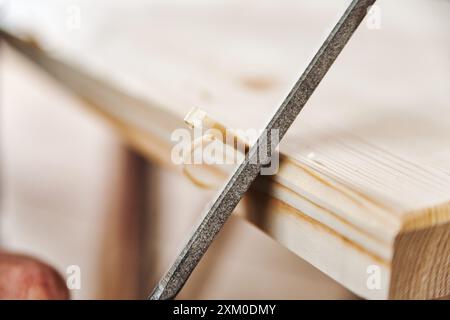 Charpentier qualifié lissant le bois dans un atelier confortable, créant des copeaux. Les mains se déplacent avec précision, en se concentrant sur les détails des meubles faits à la main. Artisan Banque D'Images