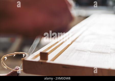 Menuisier qualifié en atelier à l'aide d'un burin pour lisser la planche de bois, créant des détails précis et des arêtes vives dans le bois Banque D'Images