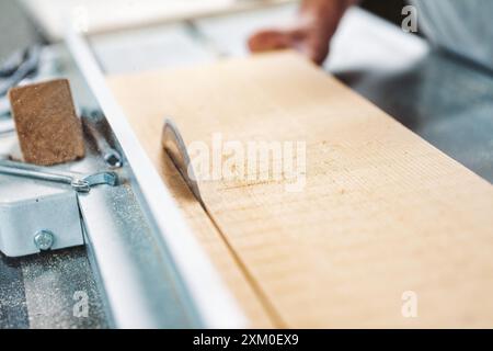 Menuisier qualifié coupant une planche de bois épaisse avec une scie circulaire dans un atelier occupé, créant une houille de sciure envoûtante. Les mains font preuve de précision et d'art, Banque D'Images