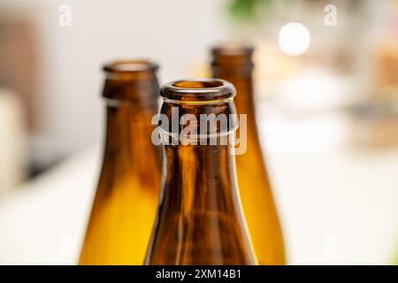 Vue détaillée de trois bouteilles en verre brun, parfaitement alignées, mettant en valeur leurs cols et leurs surfaces réfléchissantes. Idéal pour les thèmes liés aux boissons, pack Banque D'Images