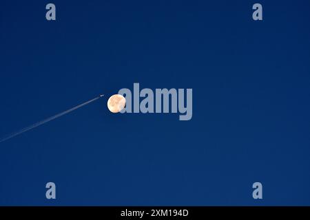 Marseille, France. 24 juillet 2024. Un avion avec sa traînée de carburant passe à travers le ciel avec la lune derrière lui. Crédit : SOPA images Limited/Alamy Live News Banque D'Images