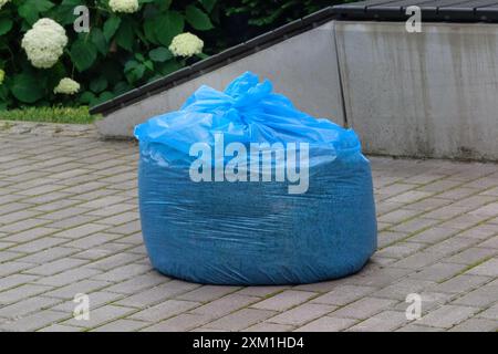 Le sac poubelle bleu est couché sur le sol. Sac plein de déchets est prêt à être envoyé au camion à ordures. Banque D'Images