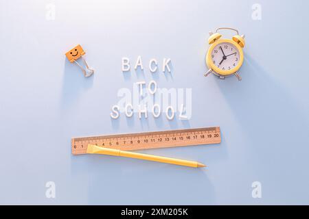 Retour à l'école. Réveil jaune, règle et stylo sur fond bleu Banque D'Images