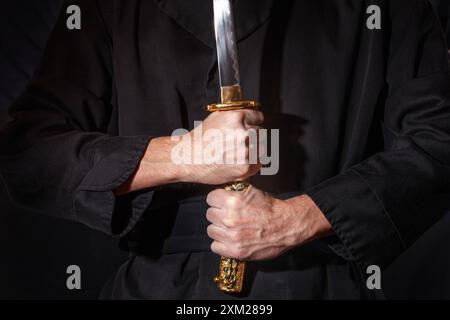 Samouraï prêt pour la bataille tenant une épée katana japonaise. Photo d'un guerrier vêtu de vêtements noirs en low key avec mise au point sélective Banque D'Images