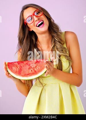 Rire, femme et portrait avec pastèque en studio pour collation d'été, confiant ou sourire avec la nutrition. Gen z modèle, fruits et verres cool sur bleu Banque D'Images