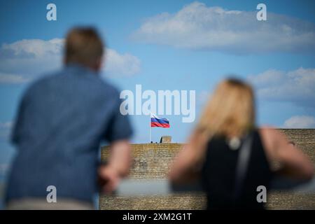 Varsovie, Pologne. 24 juillet 2024. Les gens regardent comme un drapeau russe flotte sur la forteresse Ivangorod à Narva, Estonie, le 24 juillet 2024. Les autorités estoniennes ont fermé le pont qui relie la Russie à l'Estonie pour tout le trafic entrant. Le pont de Narva est maintenant l'un des derniers endroits où les visiteurs peuvent entrer directement en Russie car le trafic aérien vers le pays a presque cessé d'exister. (Photo de Jaap Arriens/Sipa USA) crédit : Sipa USA/Alamy Live News Banque D'Images