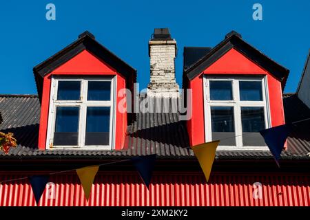 Bâtiment rouge avec lucarnes et guirlande festive contre un ciel bleu clair. Banque D'Images