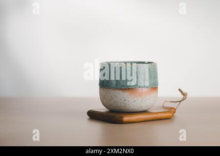 Une tasse artisanale avec du vernis sarcelle et moucheté posée élégamment sur une base en bois, illustrant la beauté minimaliste. Banque D'Images