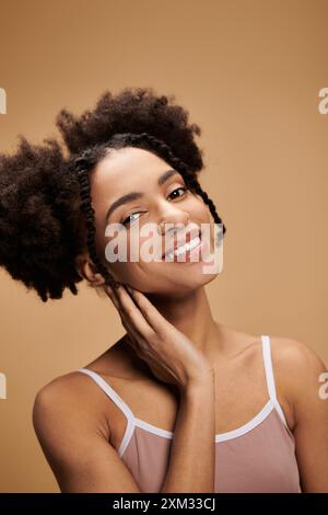 Une belle jeune femme afro-américaine avec ses cheveux dans deux petits pains sourit brillamment alors qu'elle pose sur un fond beige. Banque D'Images