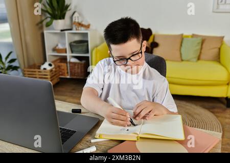 Un jeune garçon atteint du syndrome de Down est assis à une table dans sa maison, activement concentré sur son travail. Banque D'Images