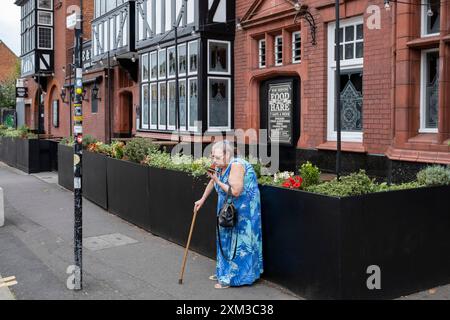 Femme sur son téléphone devant le pub Hare & Hounds le long de Kings Heath High Street le 25 juillet 2024 à Birmingham, Royaume-Uni. Kings Heath est une banlieue du sud de Birmingham, à six miles du centre-ville, et le quartier le plus proche au sud de Moseley sur l'A435 Alcester Road. La zone commerçante longe la High Street, avec des magasins, y compris des succursales de chaînes de magasins nationales, des magasins indépendants, des magasins de charité et de bonnes affaires, des supermarchés et des détaillants de vêtements. Banque D'Images