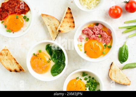 Oeufs en cocotte (oeufs cuits au four) en ramequins et toasts sur fond clair. Plat pour le petit déjeuner ou le déjeuner sain. Vue de dessus, pose à plat Banque D'Images