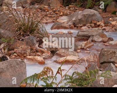 Un courant d'eau coule entre de grosses roches. L'eau est brune et trouble, et les rochers sont dentelés et rugueux. La scène est paisible et sereine, avec Banque D'Images