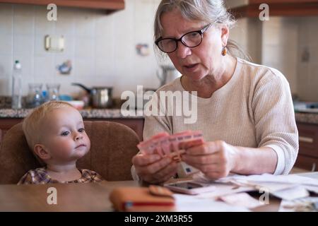 Femme senior comptant de l'argent dollars américains et euro à la maison enseignant enfant Banque D'Images