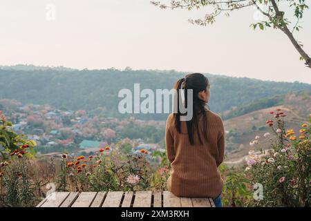 Vue arrière de la femme asiatique assise sur le banc donnant sur une belle scène rurale dans le village paisible sur la campagne à Ban Rong Kla, Phu Lom Lo Banque D'Images