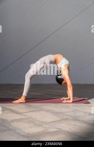 Femme brune en vêtements de sport faisant Urdhva Dhanurasana ou Up Bow pose sur un tapis de yoga à l'extérieur Banque D'Images