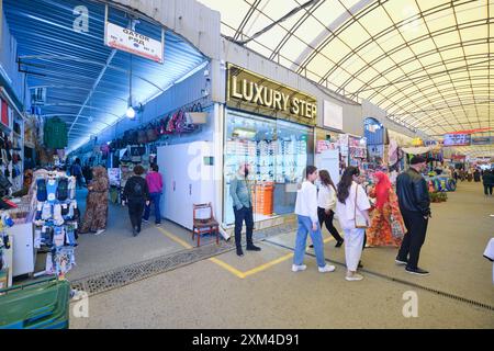 Vue sur l'une des nombreuses arcades et boutiques animées. Dans le tissu local, section vêtements du célèbre marché commercial Chorsu à Tachkent, Ouzbékistan. Banque D'Images