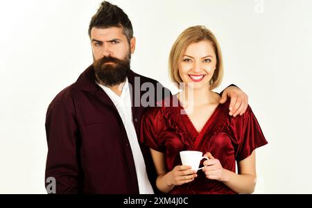 Charmant couple homme et femme en peignoir avec tasse à café le matin. Bel homme barbu embrassant sa petite amie. Jeune couple buvant du thé ou du café pour Banque D'Images