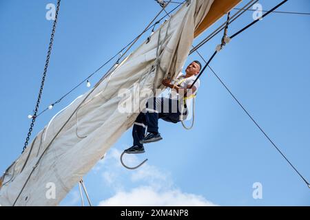 MARIEHAMN, Åland, FINLANDE - JUILLET 25 2024 : les marins grimpent haut dans le ciel pour travailler sur les voiles sur les mâts du grand voilier Guayas de l'Équateur. Deuxième jour des trois jours Åland Stage de la course de grands voiliers 2024 dans le port principal, Mariehamn, Åland, Finlande. Photo : Rob Watkins/Alamy Live News. INFO : la Tall Ships Race est un événement annuel de voile mettant en vedette des grands voiliers historiques et modernes. Il promeut l'amitié internationale et la formation des jeunes, attirant des participants et des spectateurs du monde entier pour célébrer le patrimoine maritime et l'art de la voile traditionnelle. Banque D'Images