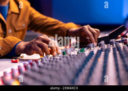 Ingénieur du son afro-américain tordant les boutons pour éditer la musique en studio, le panneau de commande d'exploitation du bureau avec faders et boutons motorisés. Producteur qualifié créant des enregistrements avec Gear. Gros plan. Banque D'Images