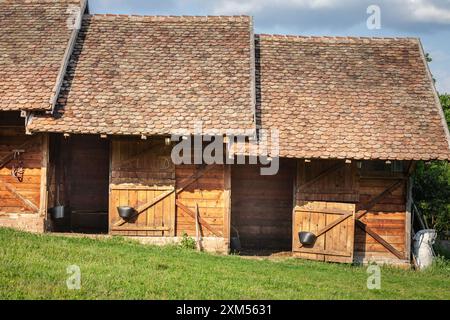 Cette image présente des écuries rustiques avec des portes en bois et un toit traditionnel en tuiles situé dans un cadre de campagne. La structure en bois refle Banque D'Images