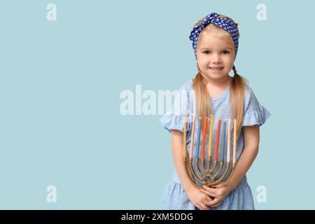 Jolie petite fille heureuse avec menorah sur fond bleu. Célébration Hanukkah Banque D'Images