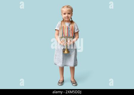 Jolie petite fille heureuse avec menorah sur fond bleu. Célébration Hanukkah Banque D'Images