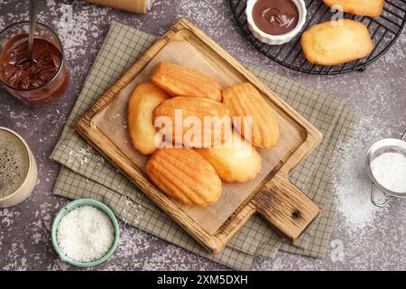 Planche en bois avec de savoureuses madeleines sur bol avec des flocons de noix de coco sur fond gris Banque D'Images