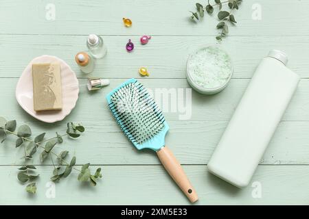 Brosse à cheveux avec des bouteilles de produits cosmétiques, savon et capsules sur fond de bois vert Banque D'Images