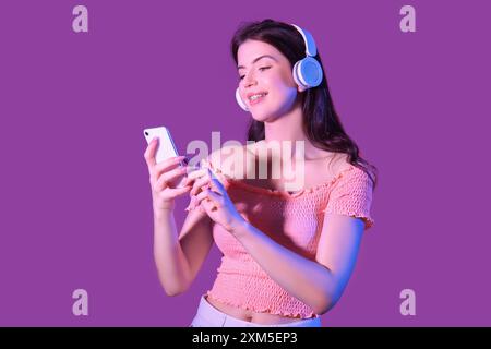 Jeune femme écoutant de la musique dans des écouteurs sur fond violet Banque D'Images