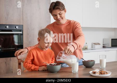 Heureux père avec son petit fils mangeant des cornflakes et buvant du lait au petit déjeuner dans la cuisine Banque D'Images