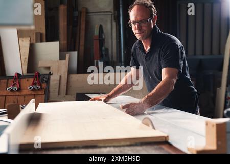 Menuisier qualifié coupant du bois avec une scie circulaire en atelier, montrant précision et passion pour la menuiserie. Création de meubles faits à la main avec dévouement Banque D'Images