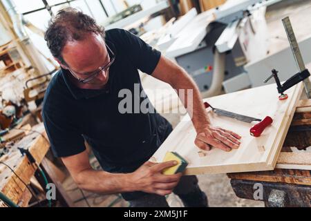 Menuisier qualifié sème le bois dans un atelier confortable, créant des surfaces lisses avec précision et expertise, mettant en valeur l'art du travail du bois Banque D'Images