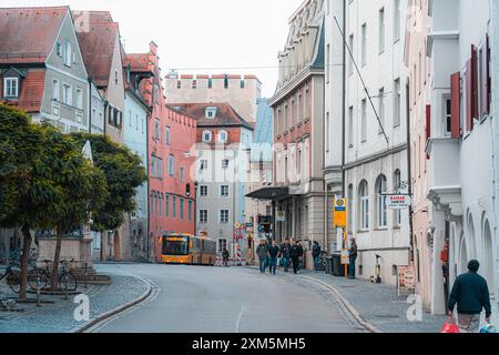 Ratisbonne, Allemagne - 06 novembre 2023 : Un bus jaune tourne à un coin d'une rue pavée à Ratisbonne, Allemagne. La rue est bordée de colorf Banque D'Images