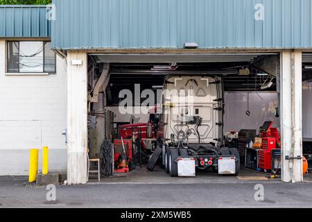 Semi-remorque grand engin de forage blanc de qualité industrielle avec capot ouvert avec un moteur éventuellement cassé debout avec des pièces démontées à l'intérieur de l'atelier de réparation attend Banque D'Images