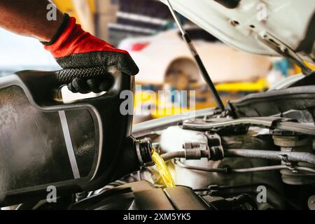 Mécanicien de voiture versant l'huile moteur dans le moteur, mécanicien change l'huile moteur dans un centre de service de réparation de voiture, concept de service d'entretien de voiture. Banque D'Images