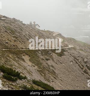 La beauté des Dolomites dévoilée : le circuit enneigé de Tre Cime en juin avec des pics jetant un œil dans le brouillard. Banque D'Images