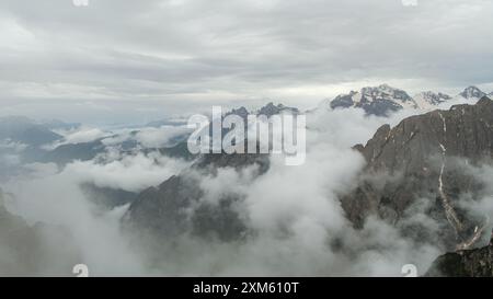 Randonnée sur le circuit enneigé de Tre Cime avec des sommets des Dolomites émergeant du brouillard en juin. Banque D'Images