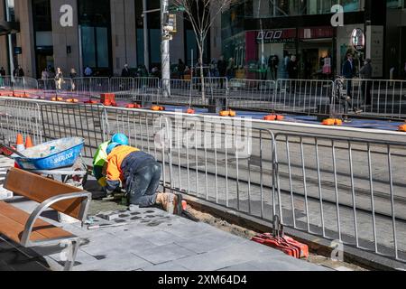 Sydney, Australie, le conseil commercial des gens qui posent un nouveau sentier le long de George Street dans le centre-ville, travaillant à genoux pour poser des dalles Banque D'Images