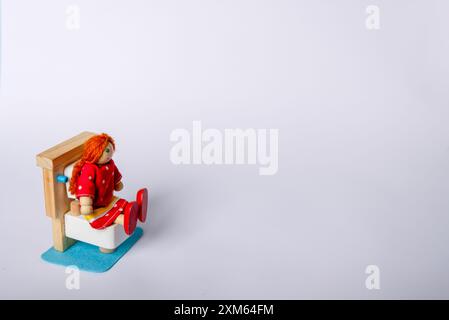 Une fille jouet en bois assise sur une toilette, placée sur un fond blanc. Cette représentation mignonne et originale capture une routine quotidienne commune Banque D'Images