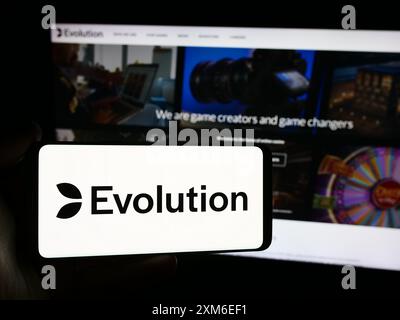 Personne tenant un smartphone avec le logo de la société suédoise de technologie de jeu Evolution AB en face du site Web. Concentrez-vous sur l'affichage du téléphone. Banque D'Images