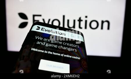 Téléphone portable avec le site Web de la société suédoise de technologie de jeu Evolution AB devant le logo de l'entreprise. Concentrez-vous sur le coin supérieur gauche de l'écran du téléphone. Banque D'Images