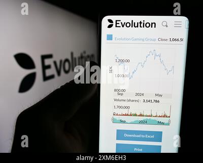 Personne tenant le téléphone portable avec la page Web de la société suédoise de technologie de jeu Evolution AB devant le logo. Concentrez-vous sur le centre de l'écran du téléphone. Banque D'Images