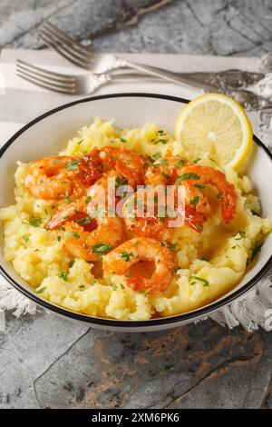 Crevettes au beurre à l'ail épicées servies avec purée de pommes de terre, citron et herbes gros plan dans un bol sur la table. Vertical Banque D'Images