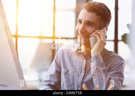 Bien sûr, nous pouvons le faire pour vous. Un jeune homme d'affaires parlant au téléphone tout en étant assis à son bureau. Banque D'Images