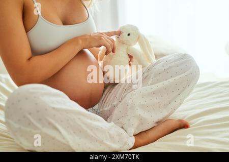 Ours en peluche, grossesse et femme sur le lit à la maison pour la liaison prénatale, la connexion ou les soins avec bébé. Jouet lapin en peluche, détente et femme enceinte Banque D'Images