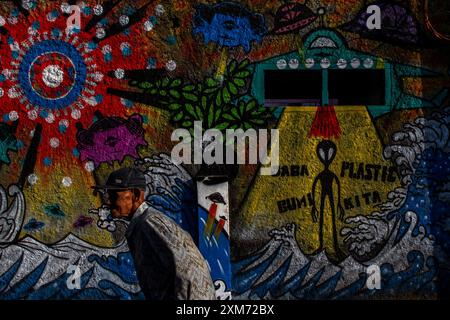 26 juillet 2024, Yogyakarta, région spéciale de Yogyakarta, Indonésie : un homme marche près d'une murale avec un OVNI et une murale sur le thème des extraterrestres dans le village des OVNIS dans le district de Mantrijeron, ville de Yogyakarta. Les résidents ont collaboré pour décorer le village avec un thème OVNI et extraterrestre pour accueillir le jour de l'indépendance de la République d'Indonésie le 17 août. En outre, le village OVNI est conçu comme un langage pour étudier l'univers, de sorte que les gens sont toujours conscients de maintenir la propreté dans leurs environnements respectifs. (Crédit image : © Angga Budhiyanto/ZUMA Press Wire/Alamy Live News) USAGE ÉDITORIAL O Banque D'Images